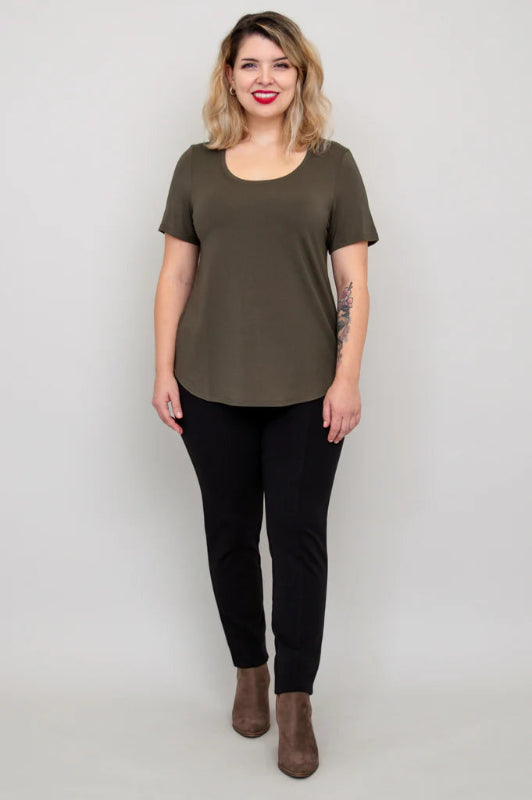 Woman wearing an olive green t-shirt and black pants on a plain background