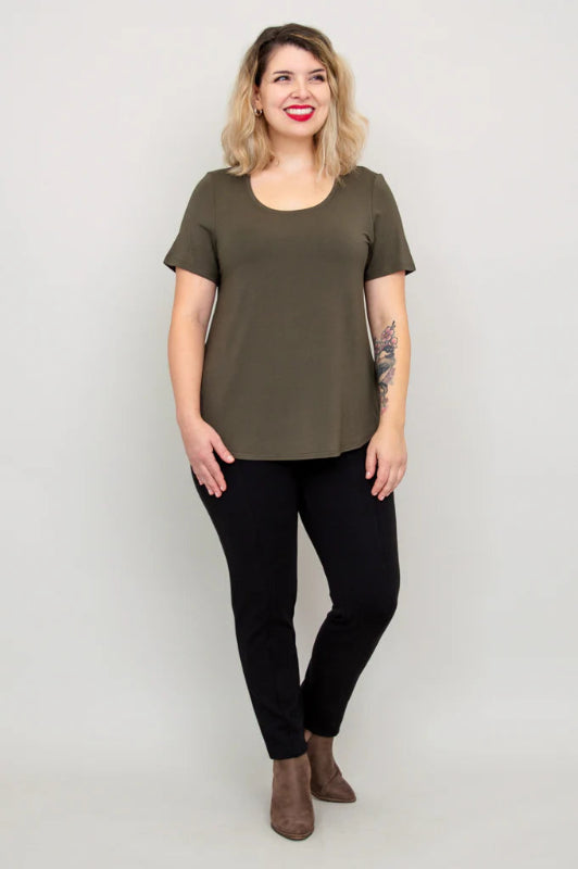 Woman wearing an olive green t-shirt and black pants against a plain background