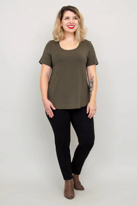 Woman wearing an olive green t-shirt and black pants against a plain background