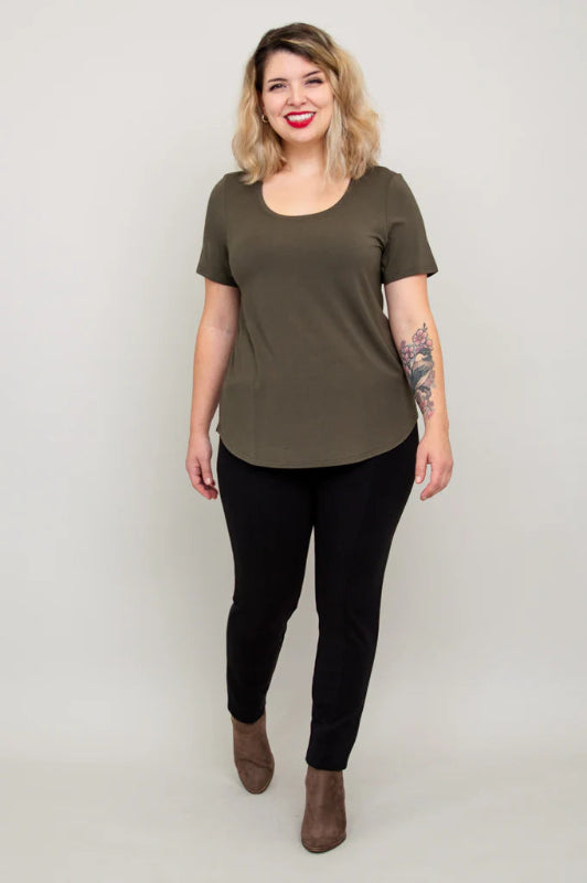 Woman wearing an olive green t-shirt and black pants on a plain background