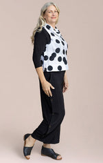 Load image into Gallery viewer, Woman wearing a black and white polka dot top with black pants on a beige background
